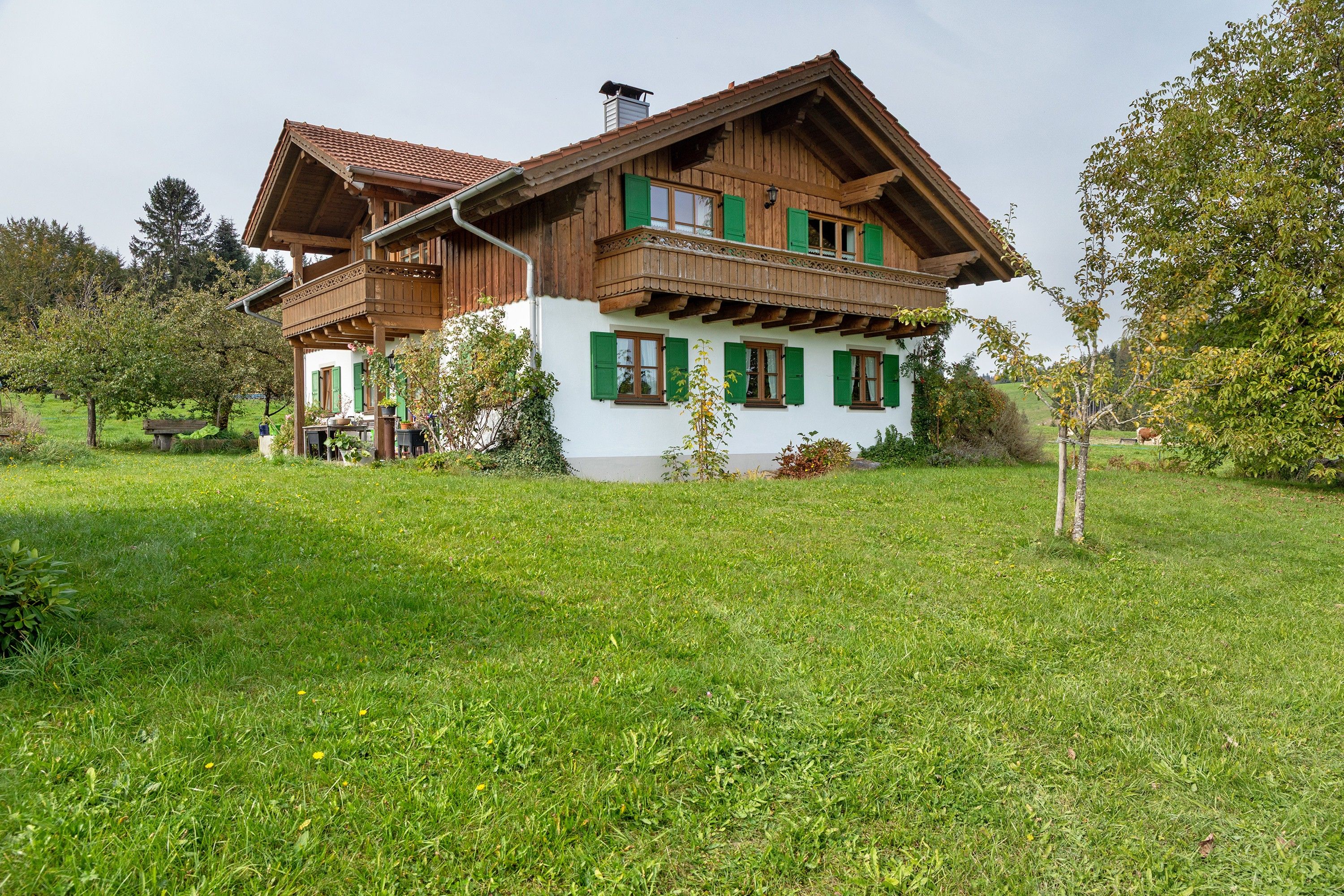 A traditional wooden house with a balcony, surrounded by a well-maintained lawn and trees.
