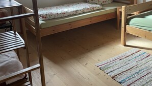 Una habitación con literas, una cama individual, una mesa de madera, una silla, una ventana con cortinas y una lámpara fijada a la pared.