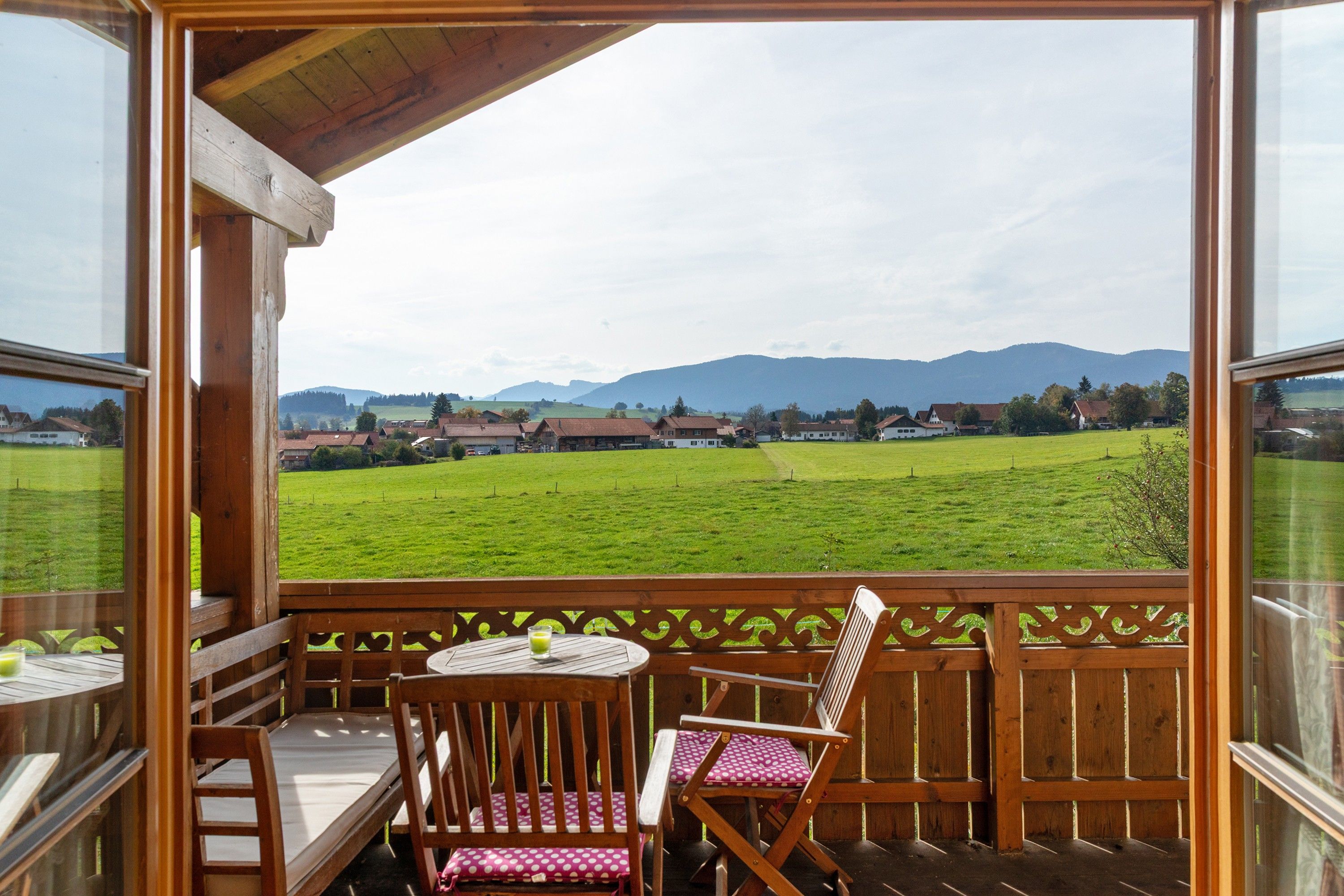 Una terraza de madera con una mesa y sillas, con vistas a un campo verde y casas a lo lejos.