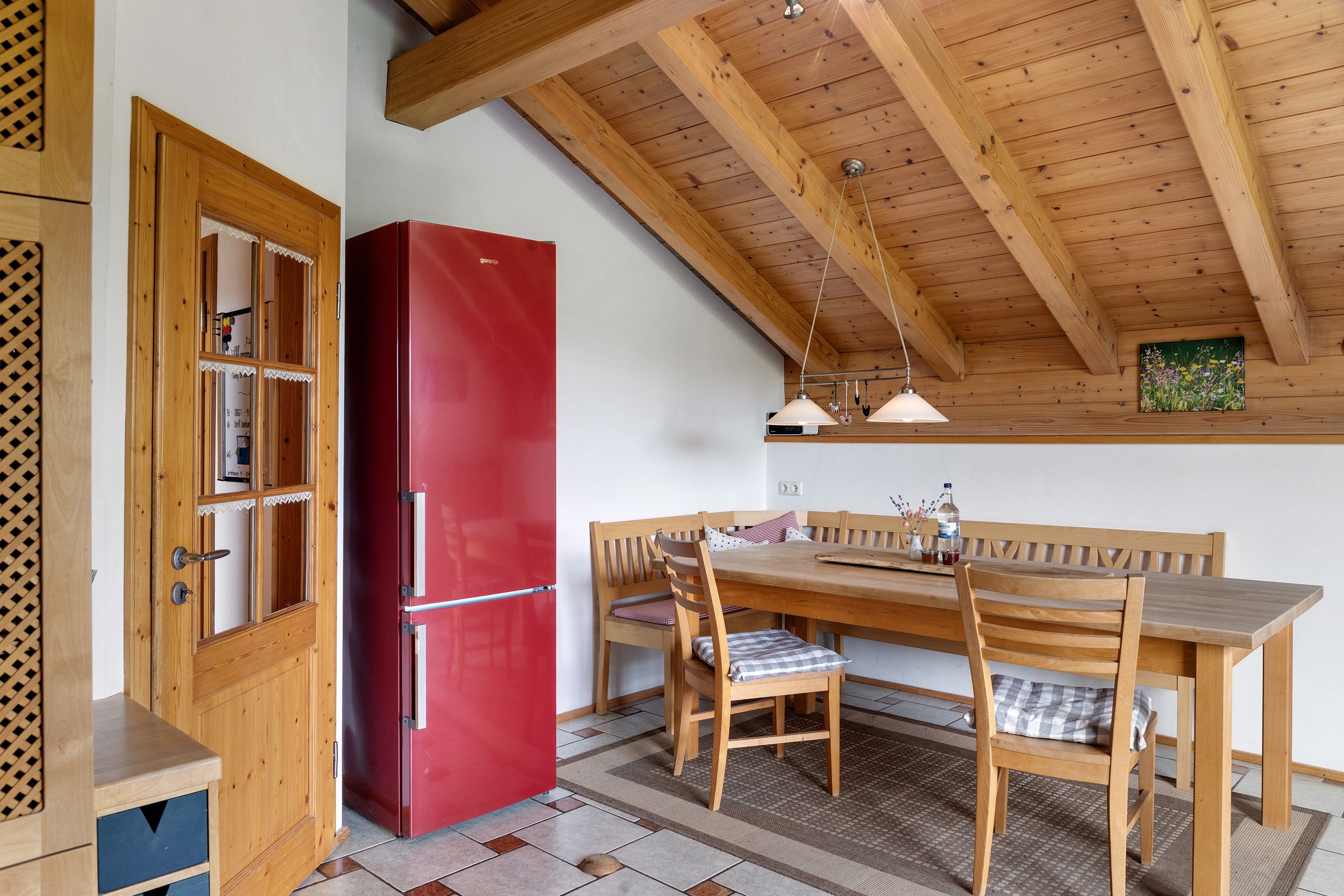 Eine Küche mit Holzboden, einem roten Kühlschrank, einem Holzessttisch mit Stühlen und einer Bank.