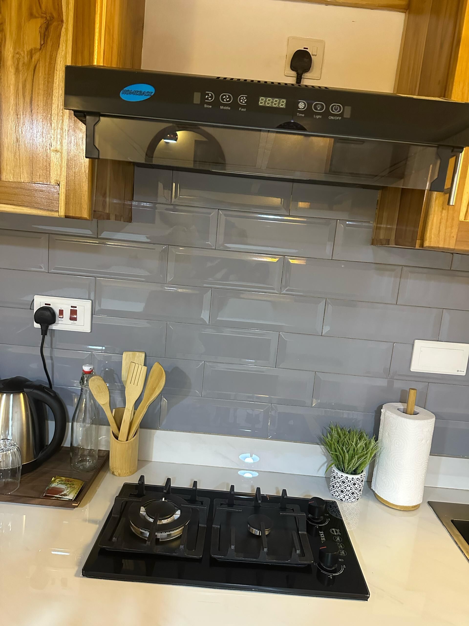 A kitchen with a black range hood, a stainless steel kettle, wooden utensils, a glass bottle, and a potted plant.
