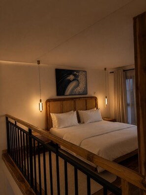 Habitació d'hotel amb un llit, un capçal de fusta, dues làmpades al costat del llit, un quadre sobre el llit i vista a l'exterior per una finestra.
