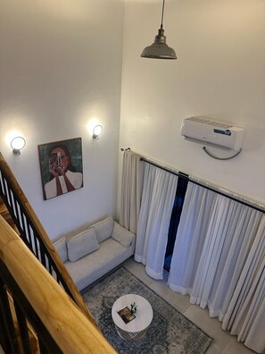 Un saló modern amb un sofà, una taula de centre rodona, un quadre, una làmpada al sostre, un aparell d'aire condicionat i una escala.