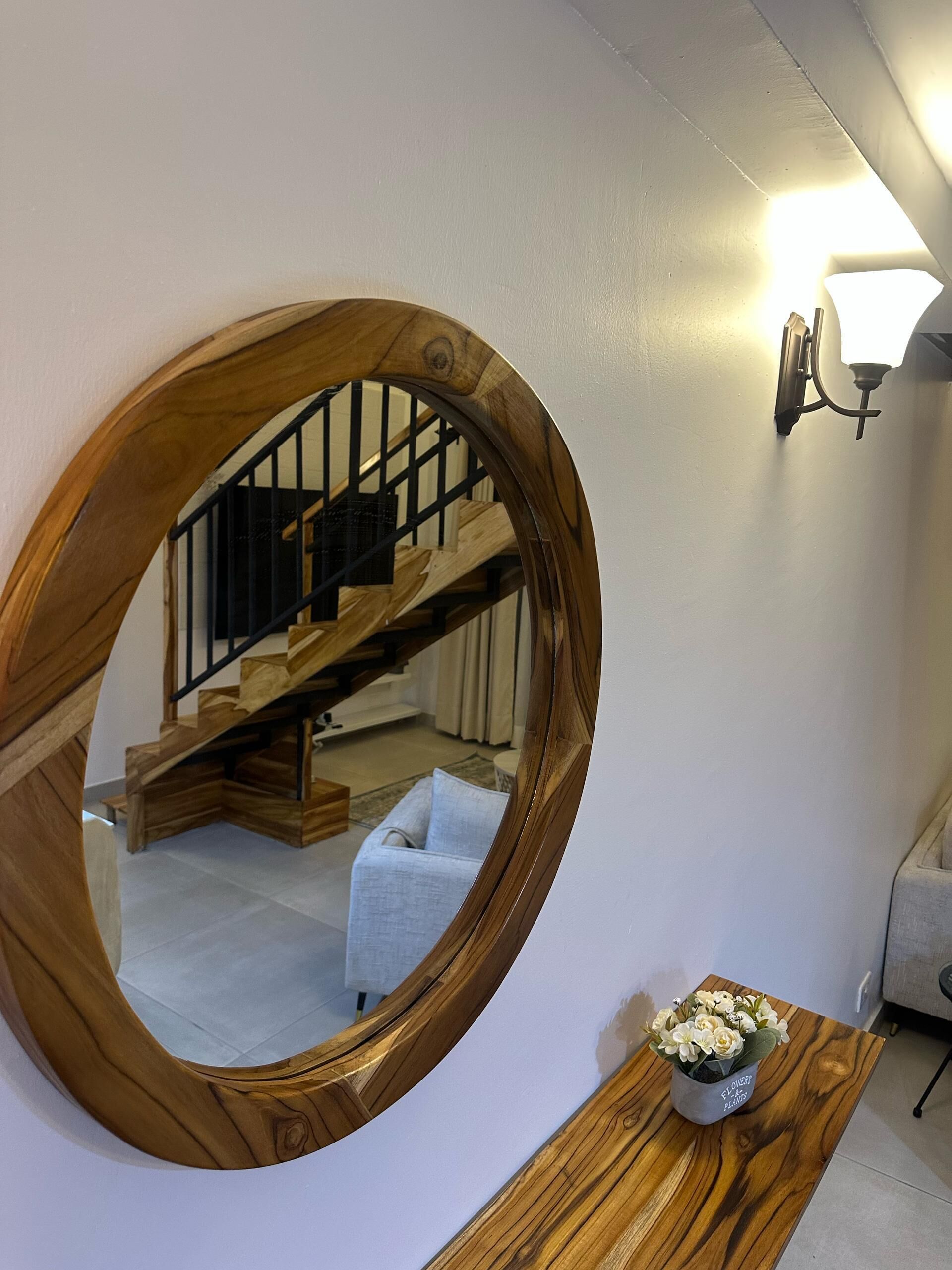 A round wooden mirror on a wall, reflecting a staircase and a light fixture.