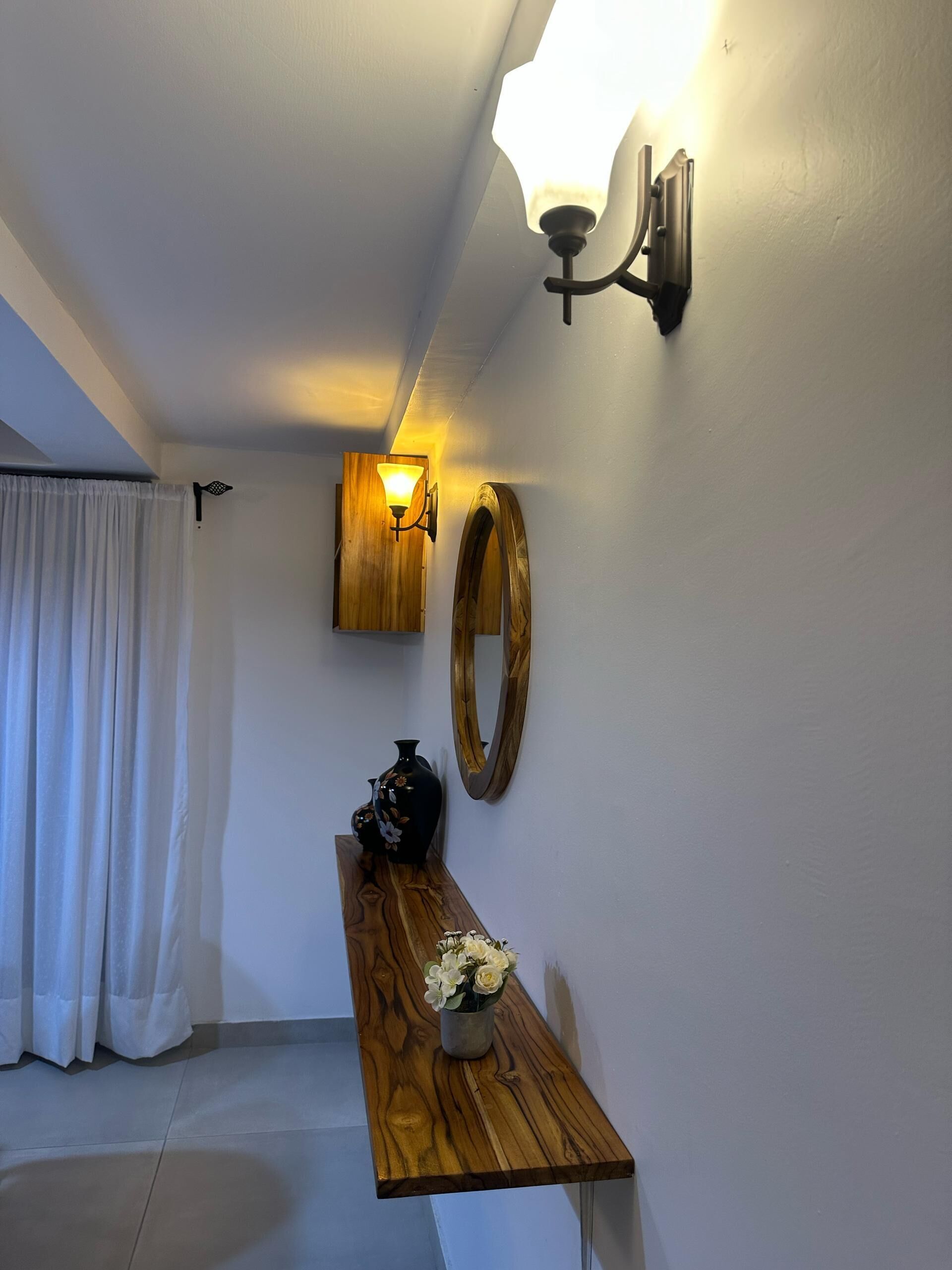 A room with a wooden console table, a wall-mounted mirror, and a wall sconce.