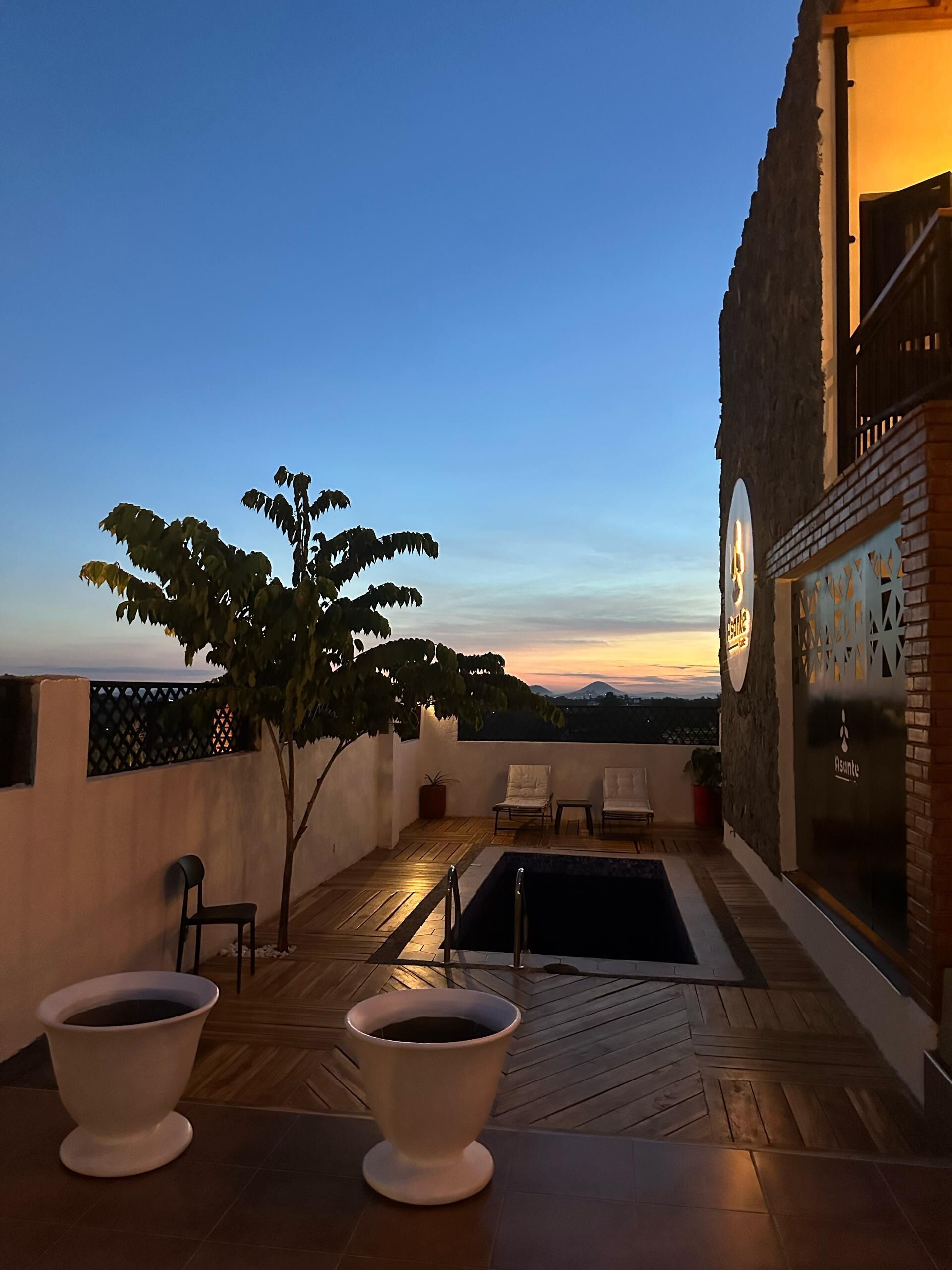 A rooftop terrace with a pool, seating area, and a view of the sunset.