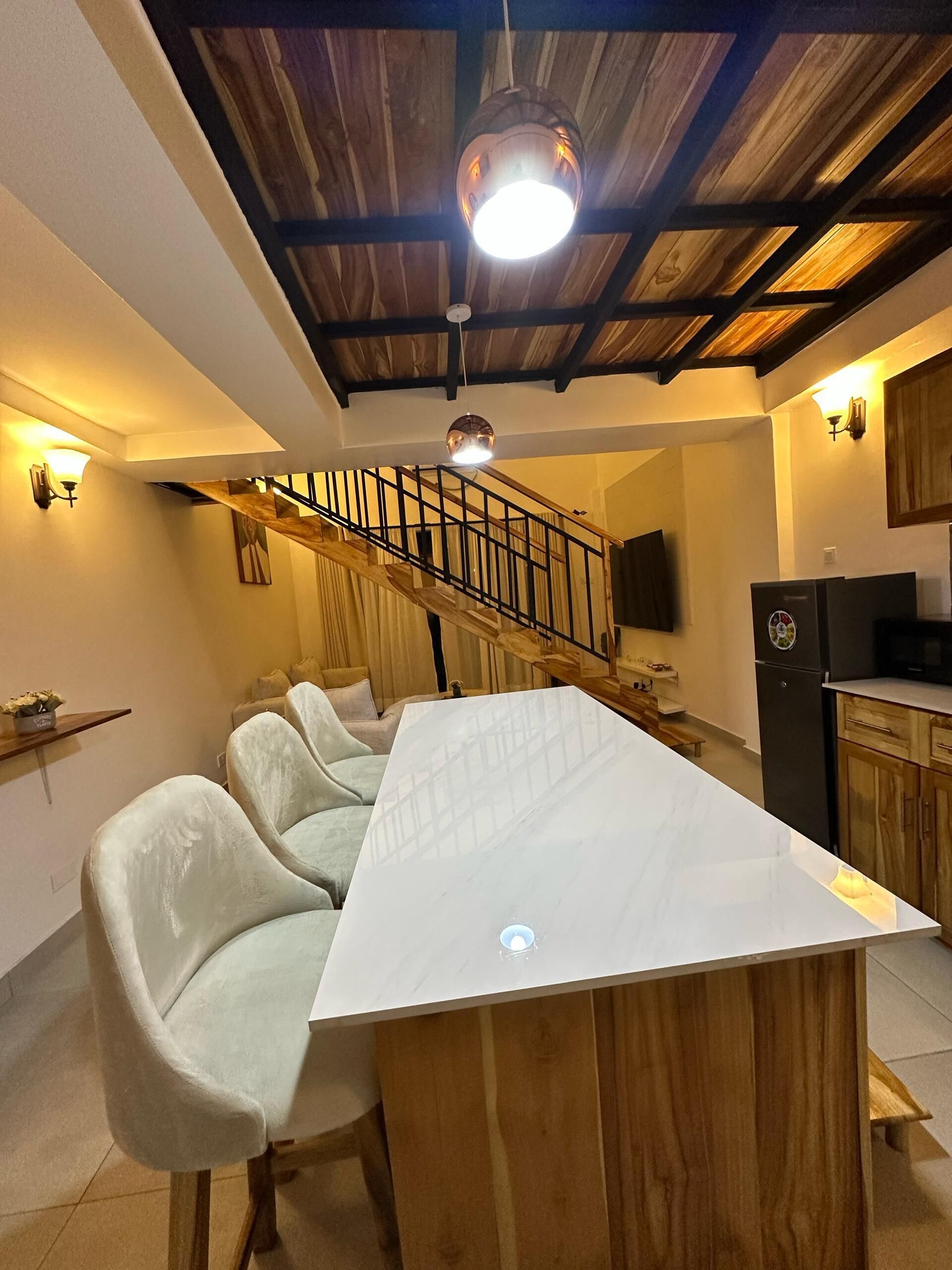A kitchen with a central island, wooden staircase, and pendant lighting.