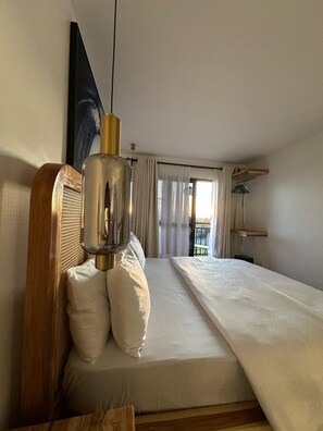 A hotel room with a bed, a hanging light fixture, a window with curtains, and a view of the outdoors.