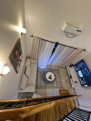 A modern living room with a sofa, a coffee table, a painting, a wall-mounted air conditioner, and a TV displaying a sports channel.