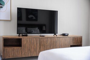Ein modernes Hotelzimmer mit einem großen Flachbildfernseher, der an einer Holzeinrichtung montiert ist, einer Fernbedienung und einem kleinen Lautsprecher auf der Einrichtung.