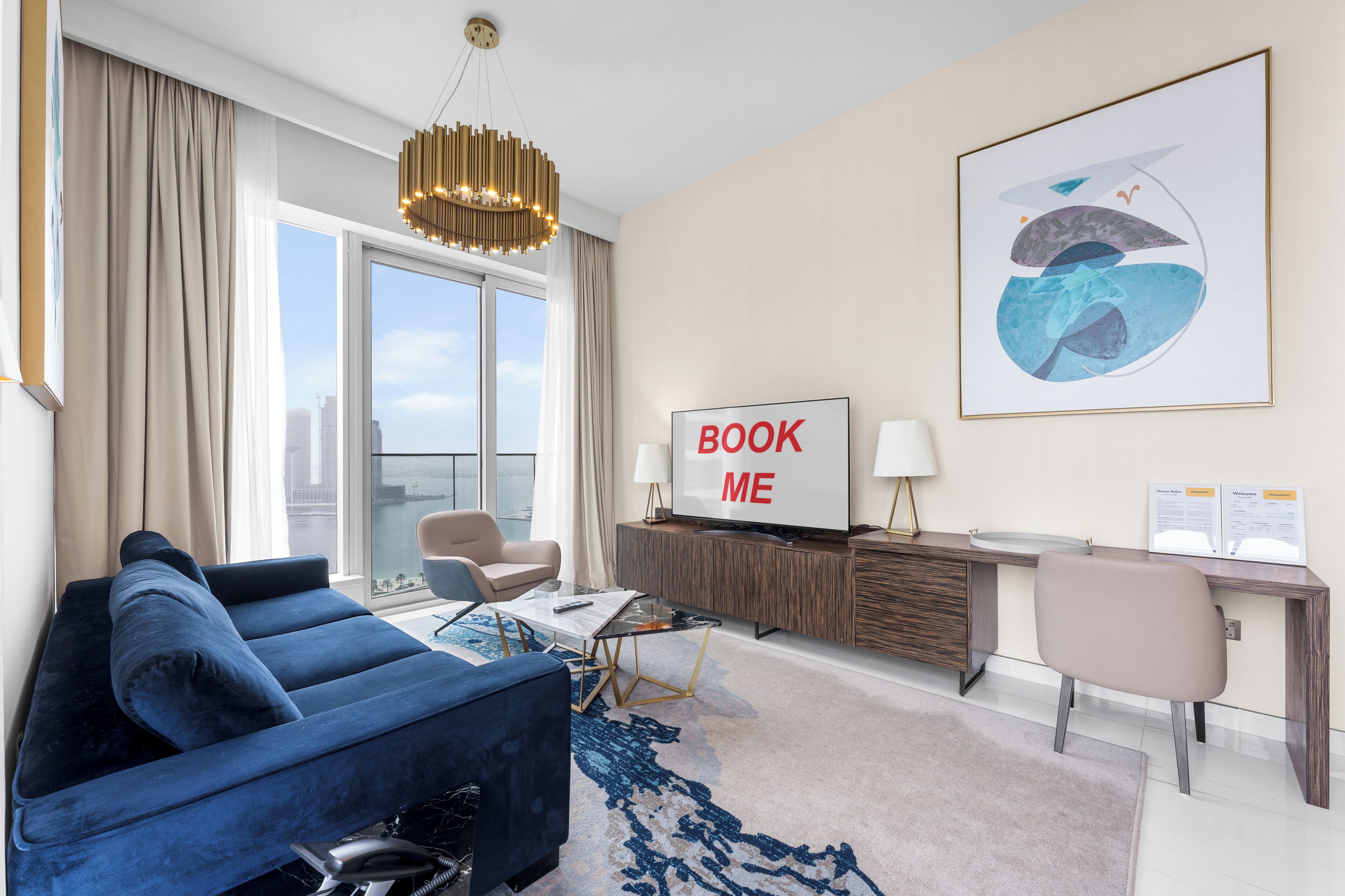 Een moderne hotelkamer met een blauwe bank, een bureau met een lamp, een groot schilderij en uitzicht op de stadsgezicht door het raam.