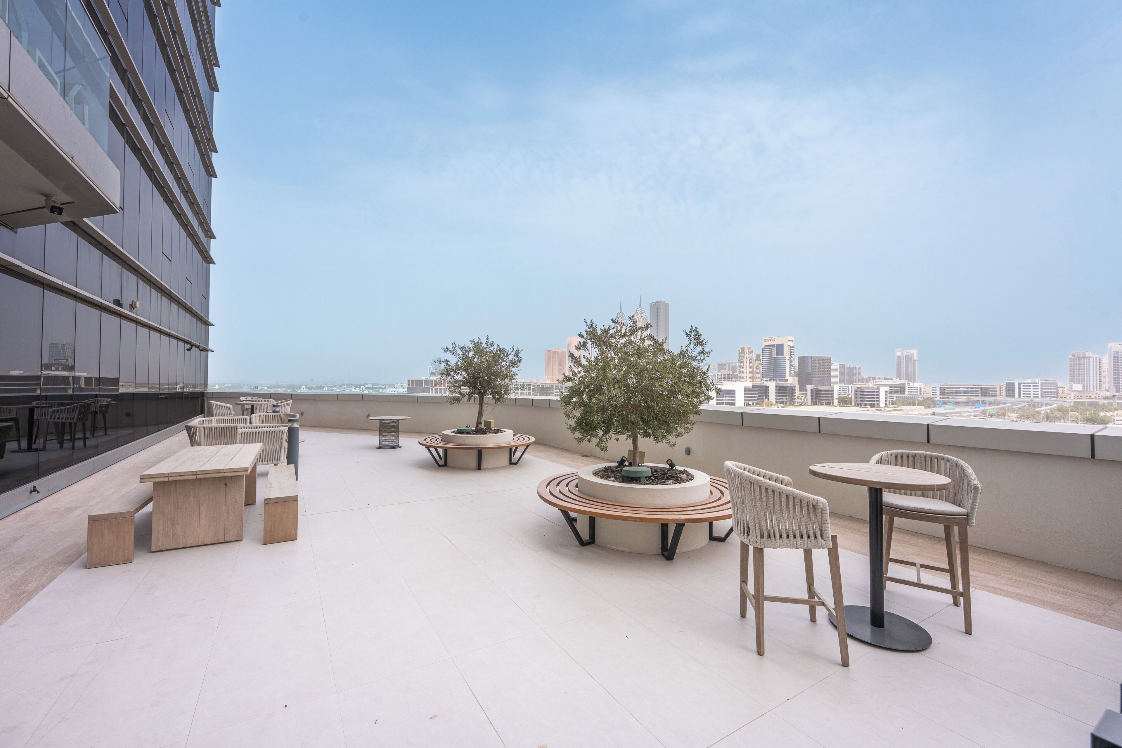 Une terrasse sur le toit avec des sièges extérieurs, un jardinier circulaire avec un arbre, et une vue sur les toits de la ville en arrière-plan.