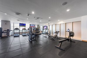 Ein Fitnessstudio mit verschiedenen Trainingsgeräten, darunter Laufbändern und Kraftmaschinen, und einem großen Bildschirm, der ein Sportevent zeigt.