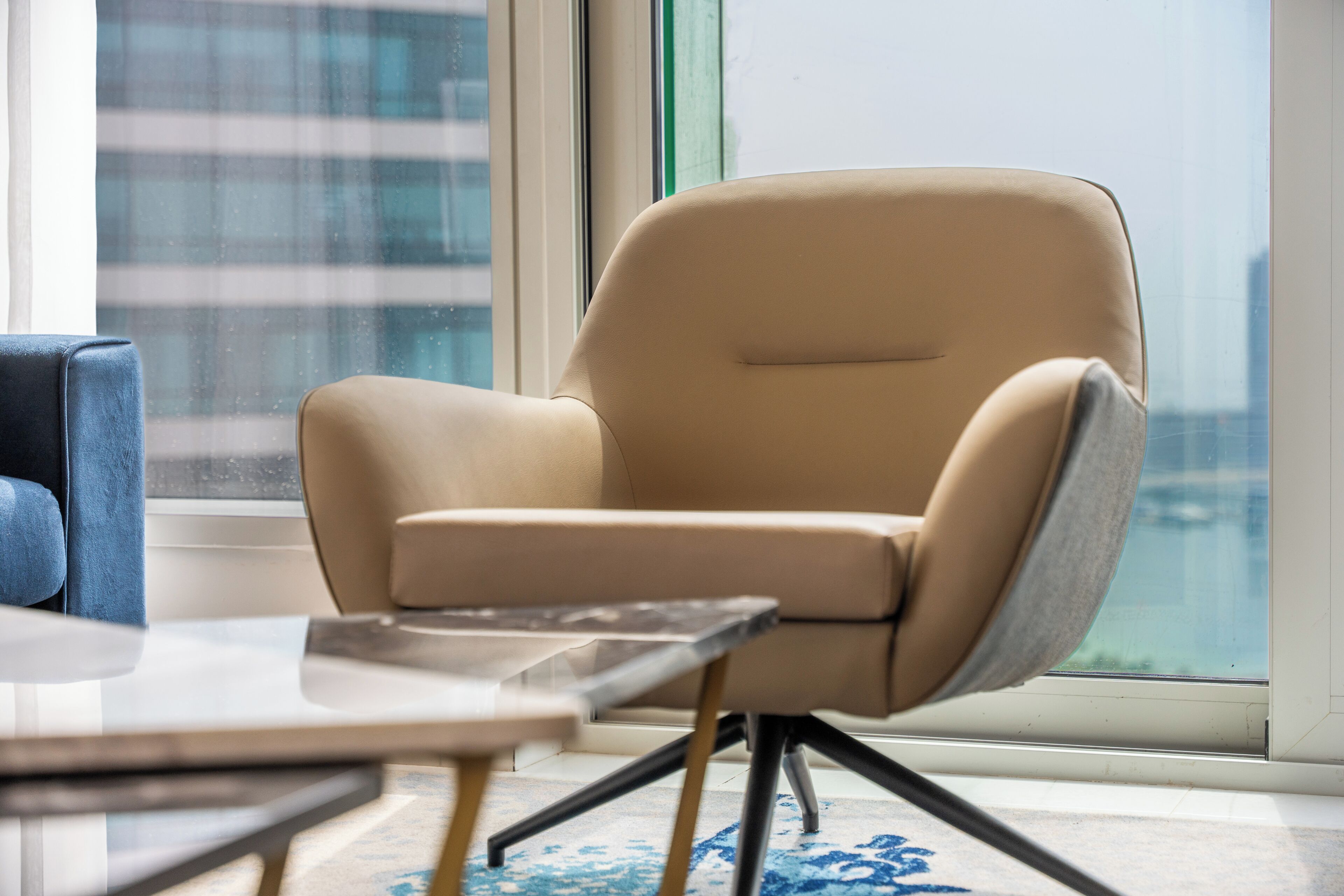 A modern chair with a high backrest and metal legs, positioned near a window with a view of a cityscape.