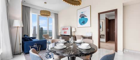 A modern hotel room with a dining area, a sofa, a large window, and a view of the city.