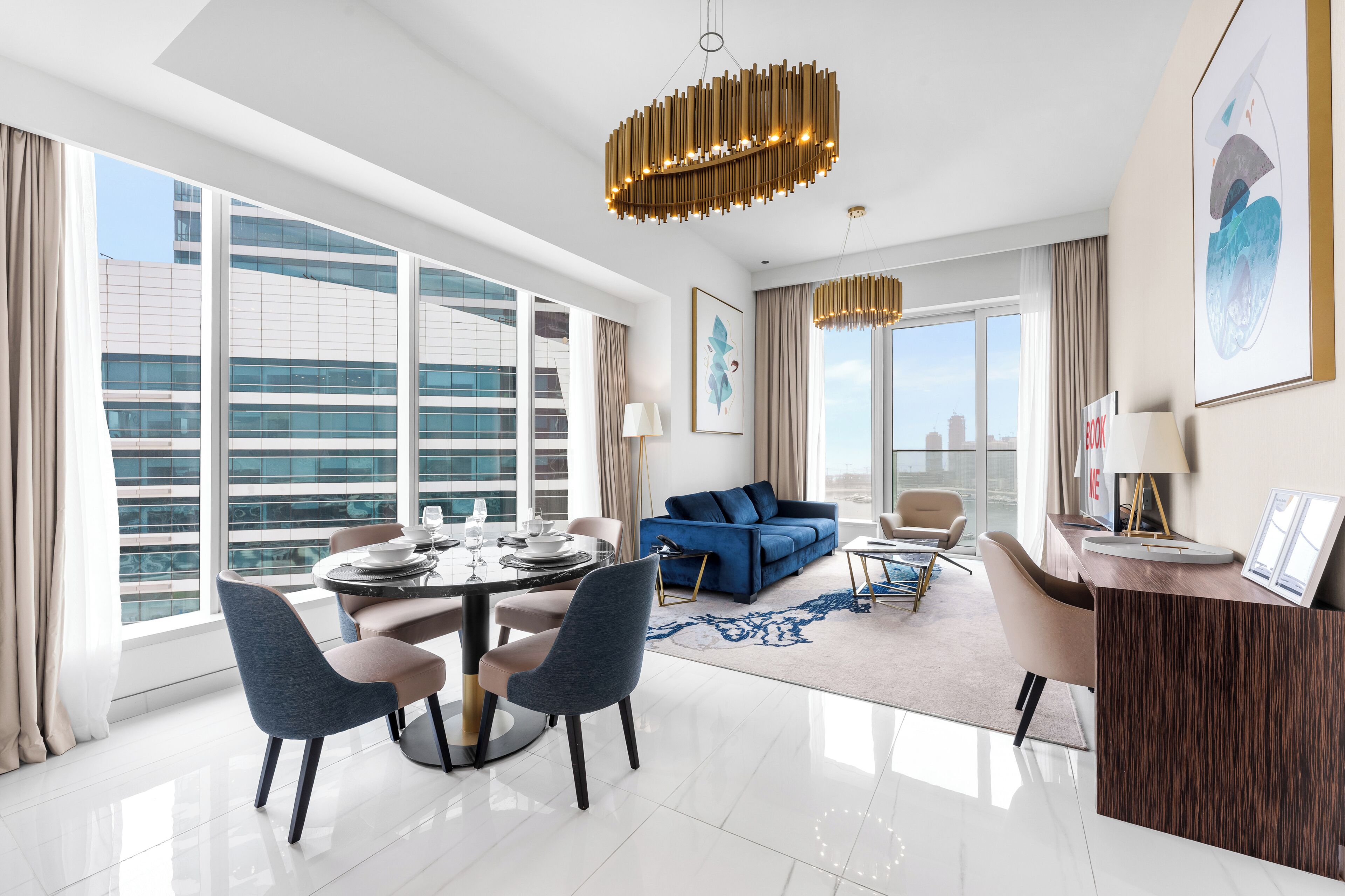 Una habitación de hotel moderna con comedor, sofá, escritorio y ventanas amplias que ofrecen vistas a la ciudad.