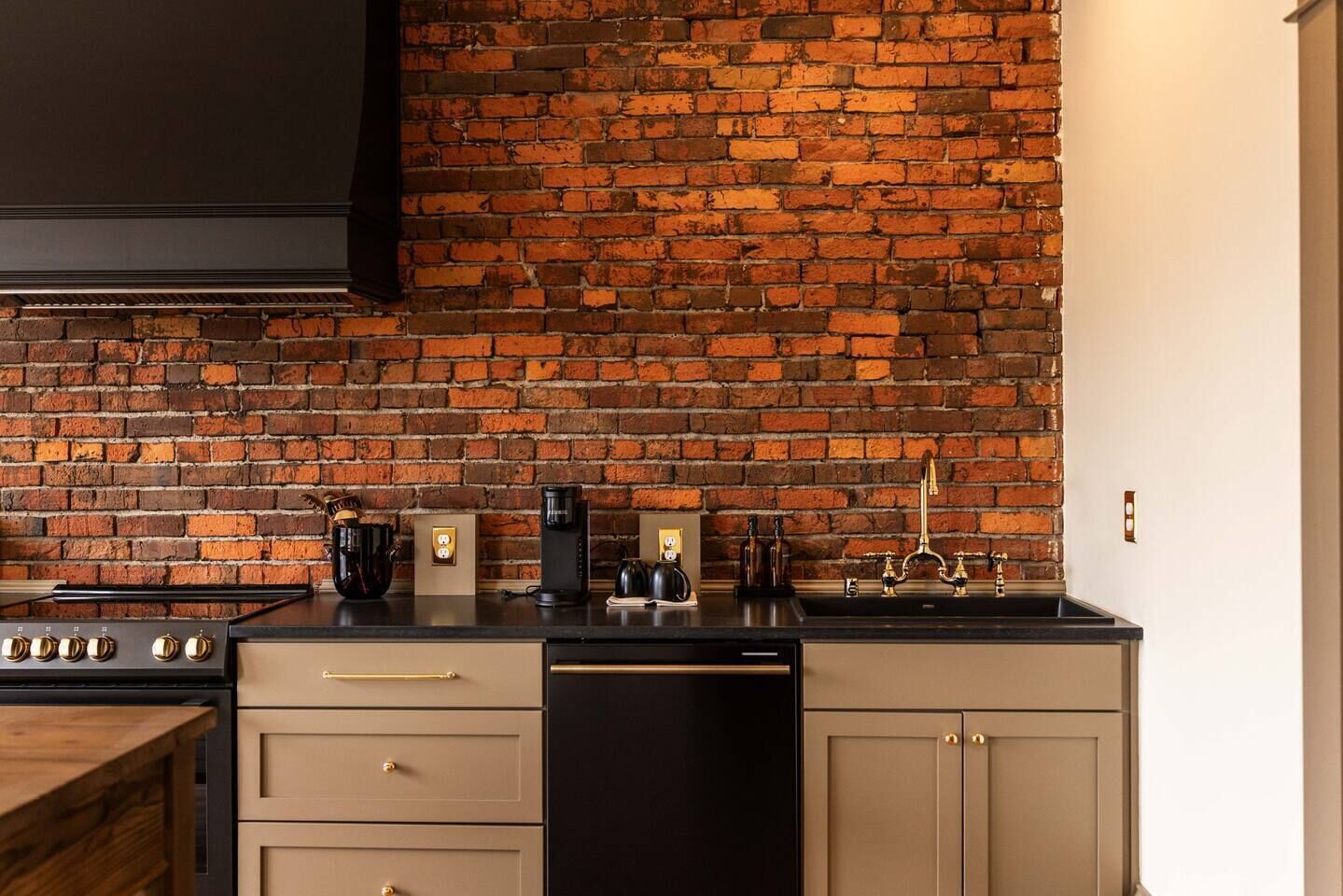 A kitchen with a brick wall, a stove, a coffee maker, and a dishwasher.