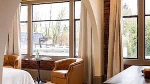 Une chambre d’hôtel avec un lit, une table en bois, une chaise et de grandes fenêtres avec des rideaux.