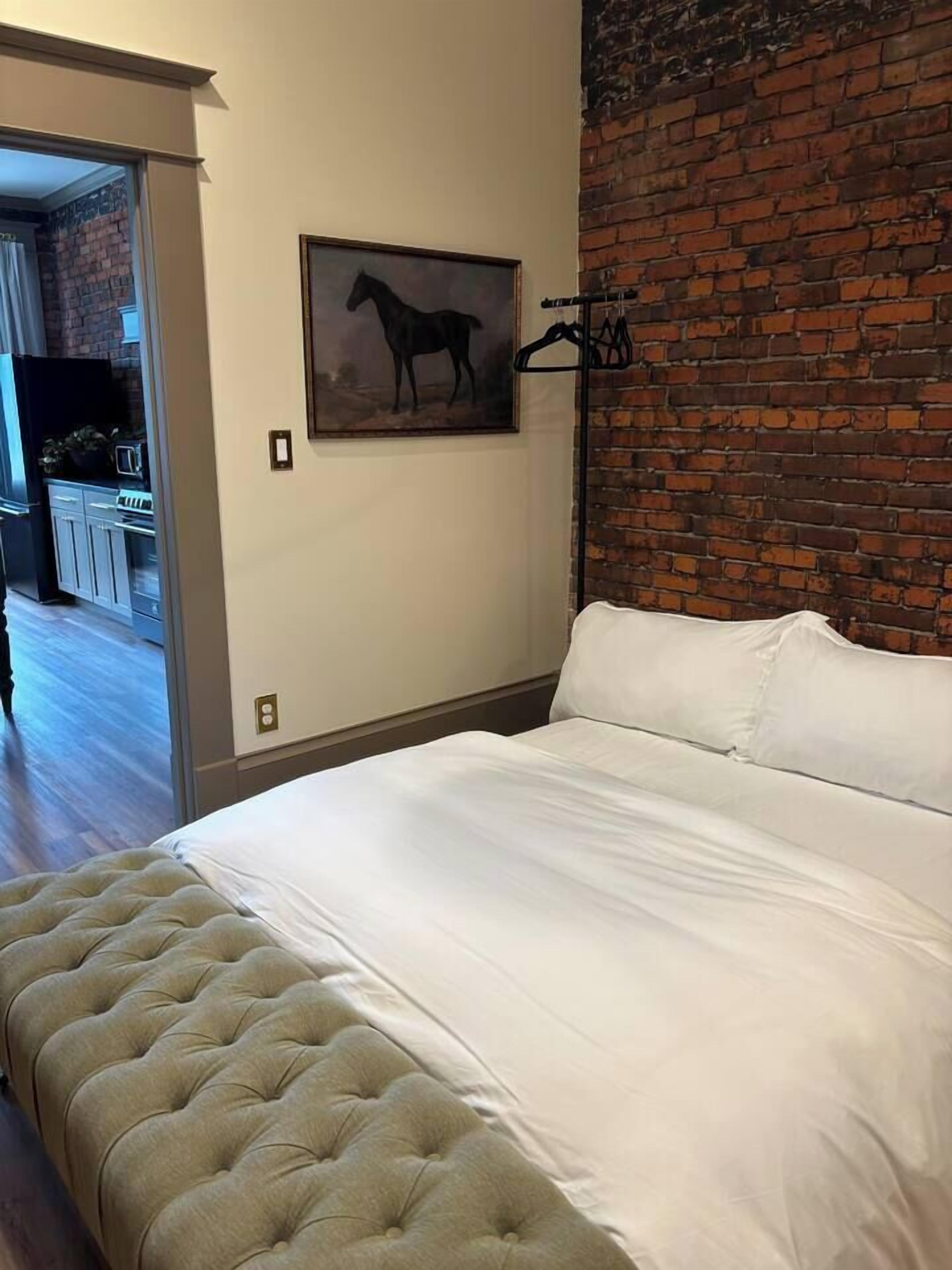 A bedroom with a large bed, a brick wall, and a painting of a horse.