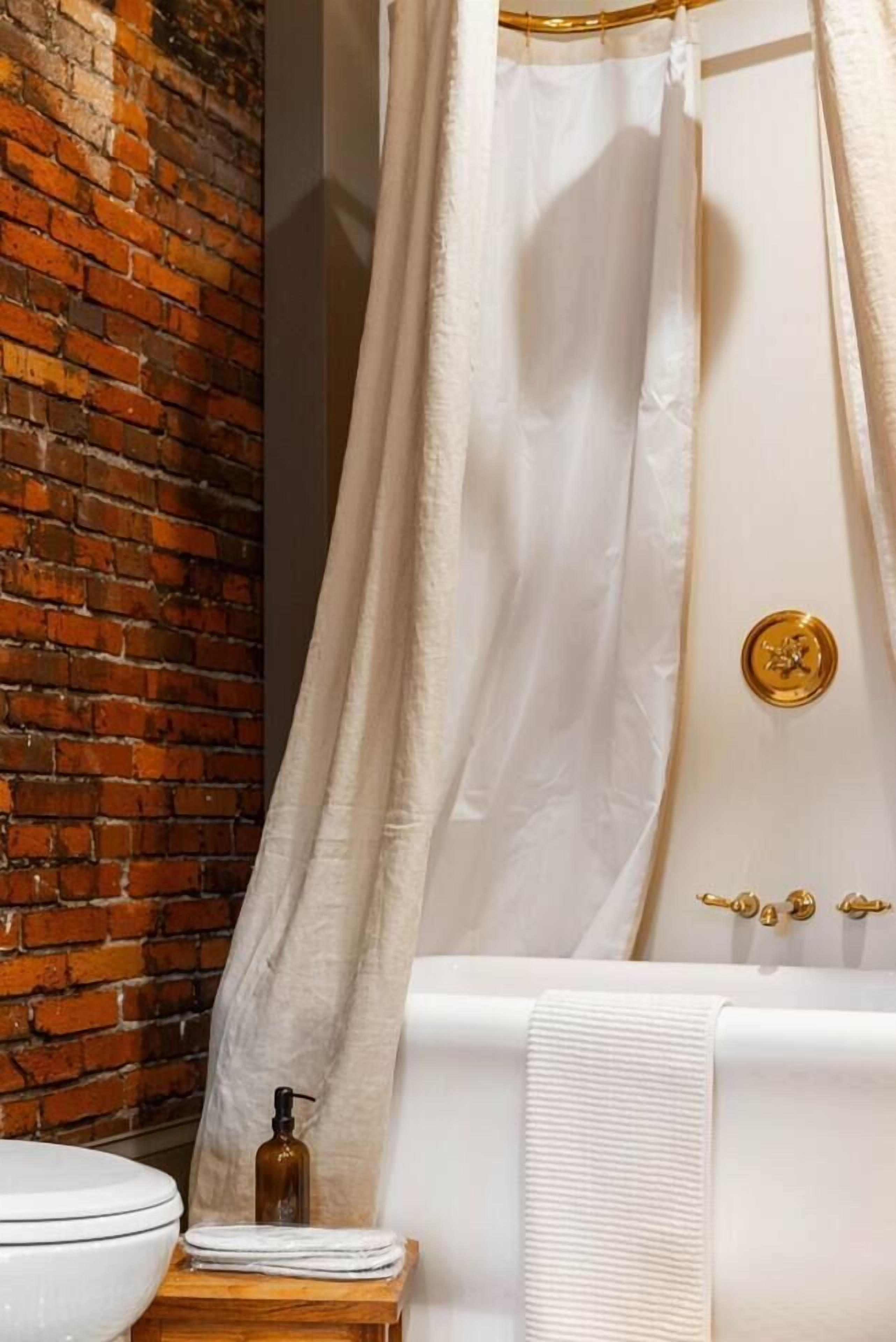 A bathroom with a white bathtub, a white toilet, a wooden stool, and a bottle of soap.