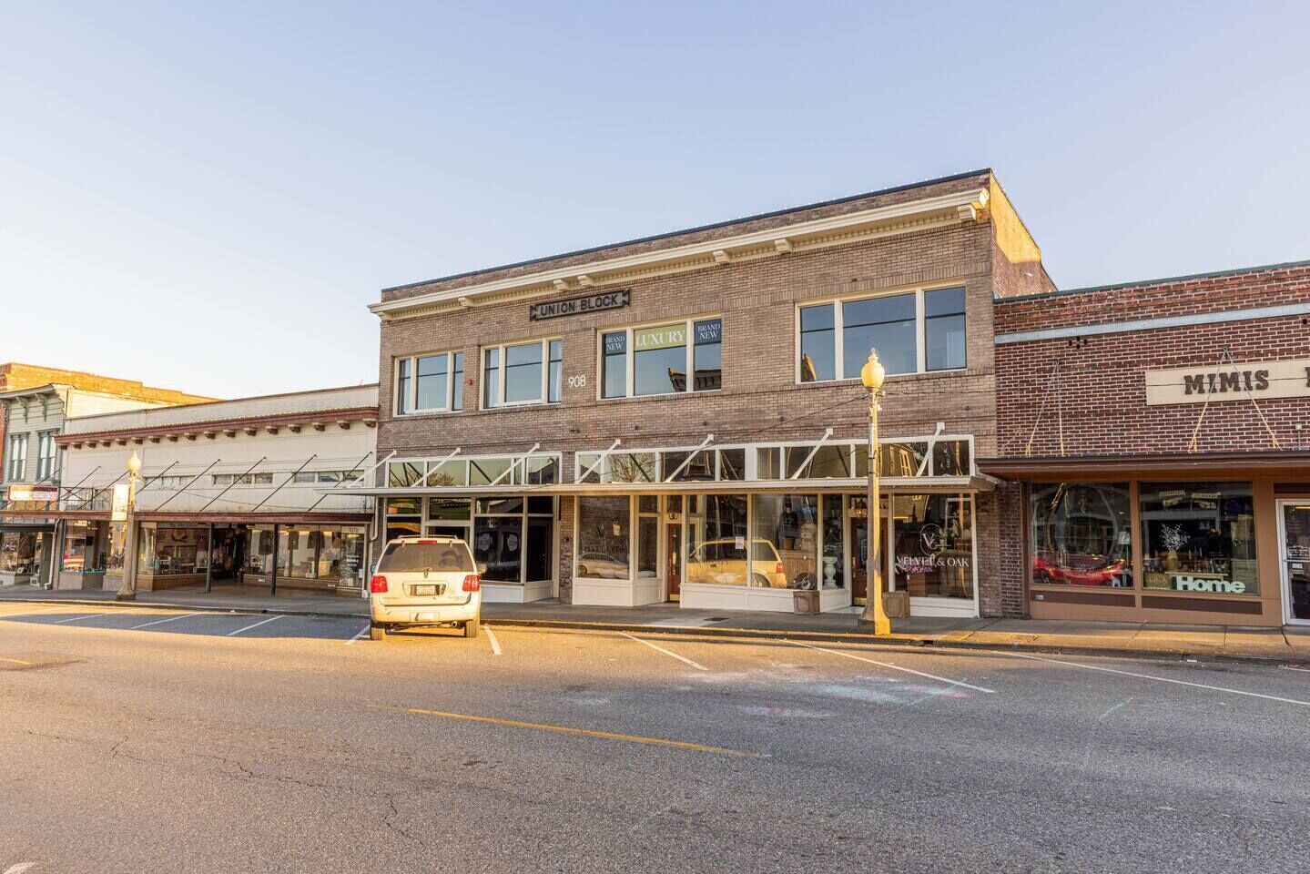 A street view of a building with a storefront labeled 'LUXURY NEW' and a car parked in front.