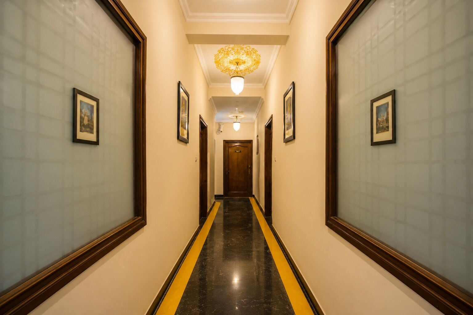 Un pasillo de hotel con cuadros en las paredes, un piso a rayas negras y amarillas, y un candelabro.