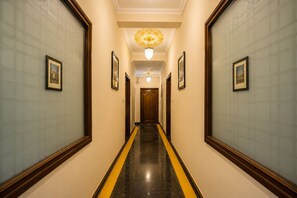 A hotel hallway with framed pictures on the walls, a black and yellow striped floor, and a chandelier. - Little Ganesha Inn (Jaipur)