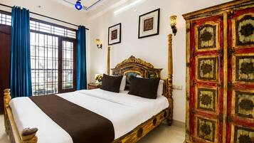 Habitación de hotel con una cama grande, un armario, una ventana con cortinas y lámparas fijadas a la pared.