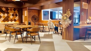 Un comedor moderno con mesas y sillas de madera, un ventilador y un arreglo floral decorativo.