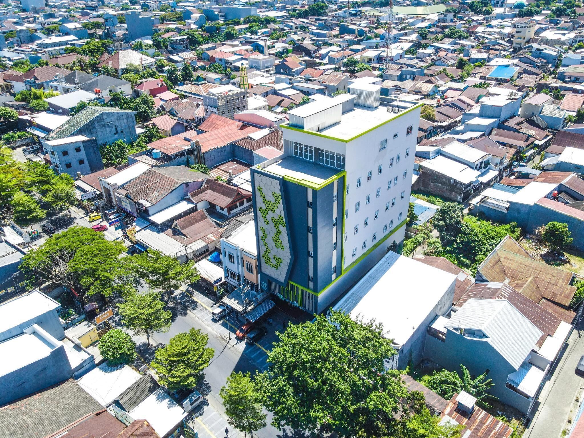 Un edificio moderno con una fachada geométrica distintiva, rodeado por una zona urbana densa con edificios tradicionales.