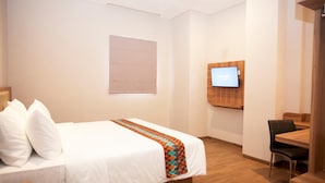 Una habitación de hotel con una cama, televisión montada en la pared y una mesa de madera con sillas.