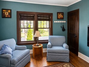 A room with two armchairs, a small side table with a lamp, a wooden door, and a window with blinds. - Classic Fargo Retreat Near NDSU & Downtown (Fargo)