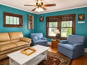 A living room with a brown leather sofa, two blue armchairs, a white coffee table, and a ceiling fan. - Classic Fargo Retreat Near NDSU & Downtown (Fargo)