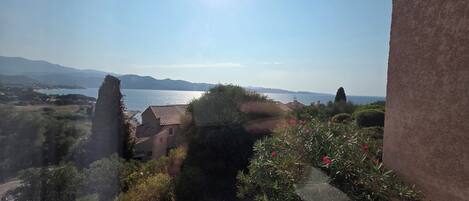Eine Küstenlandschaft mit freiem Blick auf das Meer, entfernten Bergen und einem Gebäude mit Ziegeldach.