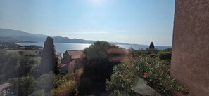 A coastal landscape with a clear view of the sea, distant mountains, and a building with a tiled roof. - One-bedroom apartment right on the water, 5 minutes from St. Florent. (Patrimonio)