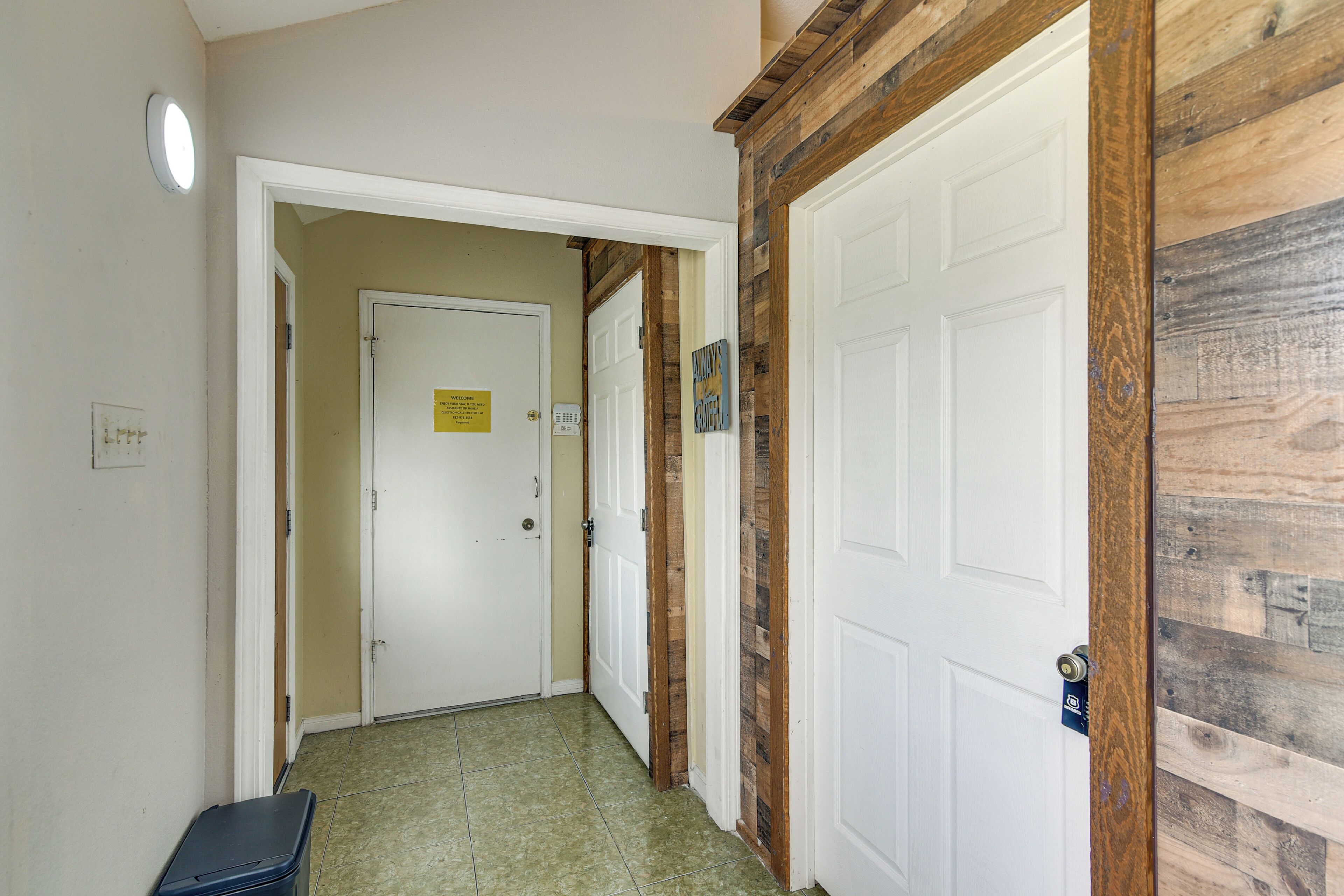 A hallway with a white door, a wooden accent wall, and a trash bin.