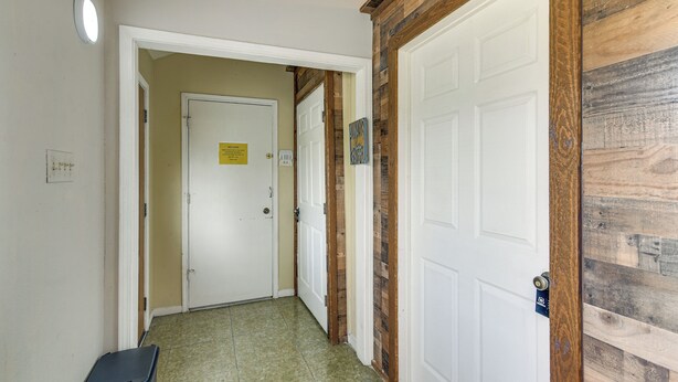 Un pasillo con una puerta blanca, un revestimiento de madera y un basurero.