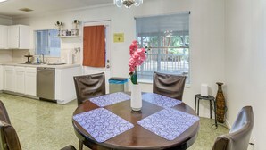 Un comedor con una mesa redonda, sillas, un florero con flores y una cocina al fondo.