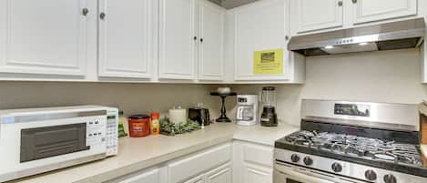 A kitchen with white cabinets, a stainless steel stove, a microwave, and a coffee maker.