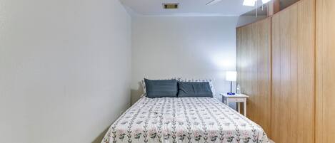 A bedroom with a bed, a ceiling fan, a nightstand, and a wooden wardrobe.