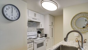 A kitchen with white cabinets, a stove, a sink, and a clock on the wall. - Unwind Poolside, Walk to Shore! Orange Beach Condo (Orange Beach)