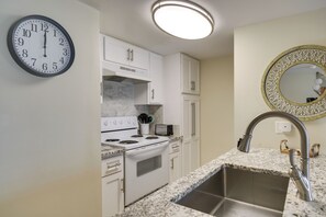 A kitchen with white cabinets, a stove, a sink, and a clock on the wall. - Unwind Poolside, Walk to Shore! Orange Beach Condo (Orange Beach)