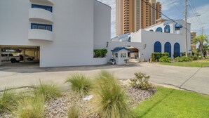 A modern building with a white facade, a parking garage, and a tall residential building in the background. - Unwind Poolside, Walk to Shore! Orange Beach Condo (Orange Beach)