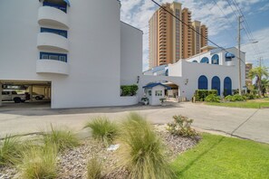 A modern building with a white facade, a parking garage, and a tall residential building in the background. - Unwind Poolside, Walk to Shore! Orange Beach Condo (Orange Beach)