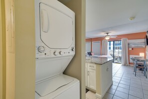 A laundry area with a washing machine, a kitchen with a dining area, and a balcony with a view. - Unwind Poolside, Walk to Shore! Orange Beach Condo (Orange Beach)