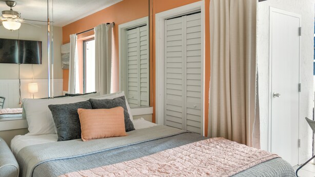 A bedroom with a bed, a ceiling fan, a TV, and a window with shutters. - Unwind Poolside, Walk to Shore! Orange Beach Condo (Orange Beach)
