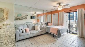A hotel room with a sofa, a bed, a ceiling fan, a large mirror, and a view of the outside. - Unwind Poolside, Walk to Shore! Orange Beach Condo (Orange Beach)