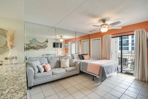A hotel room with a sofa, a bed, a ceiling fan, a large mirror, and a view of the outside. - Unwind Poolside, Walk to Shore! Orange Beach Condo (Orange Beach)