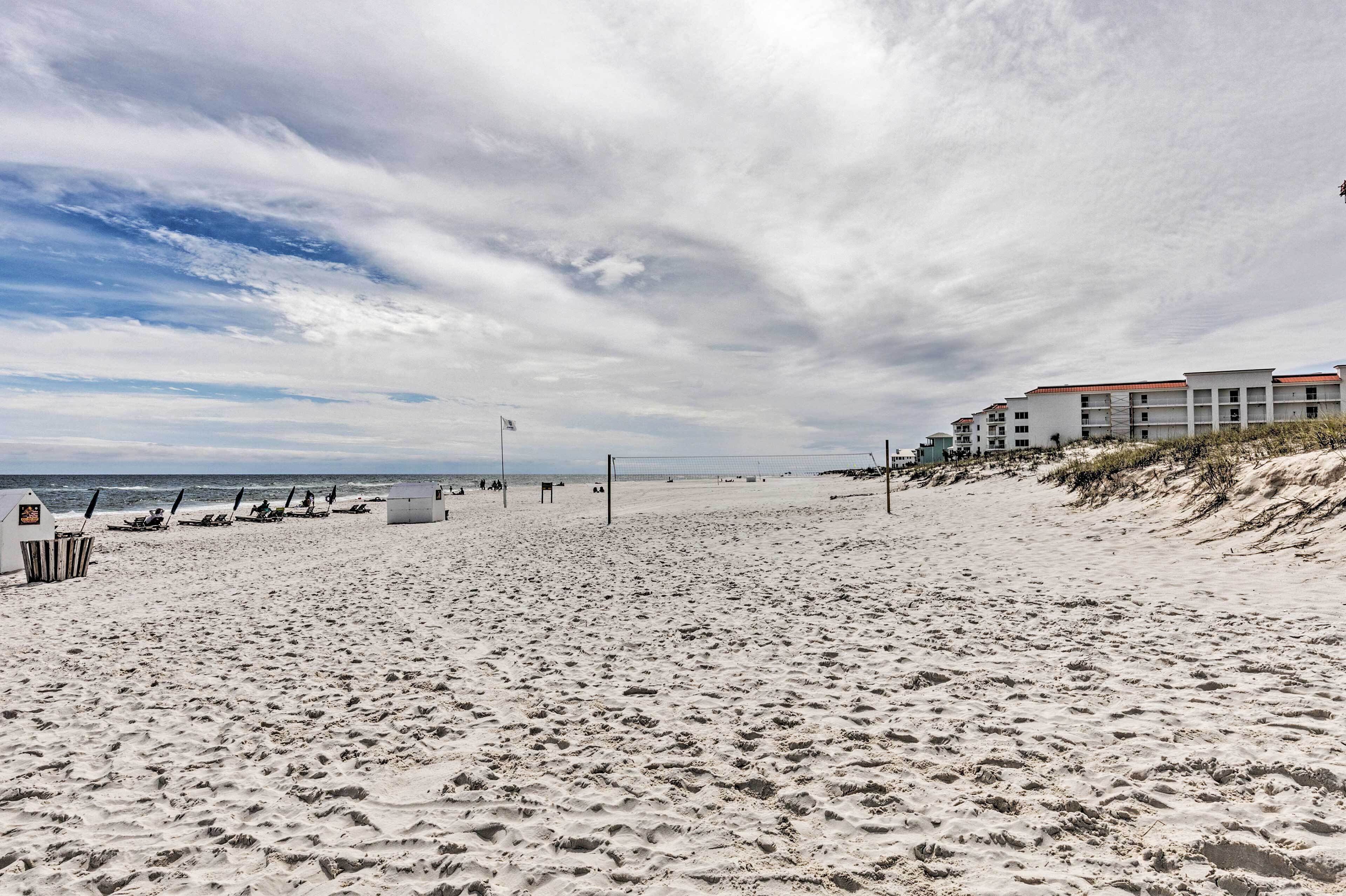 A beach with a row of buildings, a volleyball net, and a lifeguard tower.