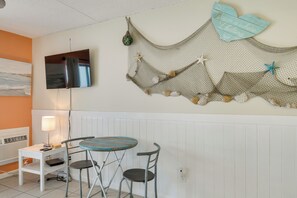 A room with a white wall, a TV mounted above a whiteboard, a small table with two chairs, and a decorative wall hanging with a starfish and text. - Unwind Poolside, Walk to Shore! Orange Beach Condo (Orange Beach)